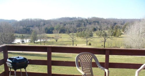 A scenic view from a deck, featuring a grill and rolling hills with trees under a clear blue sky.