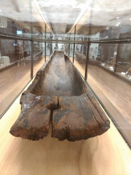 A wooden artifact displayed in a glass case, showcasing its weathered surface and historical significance.