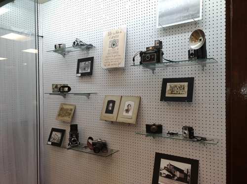 A display case featuring vintage cameras, photographs, and a book on shelves against a dotted background.
