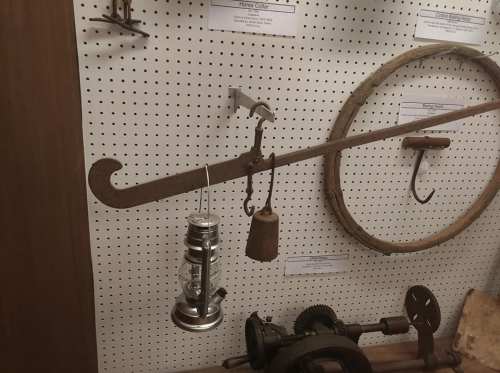 A vintage tool display featuring a lantern, bell, and curved hook on a pegboard background.