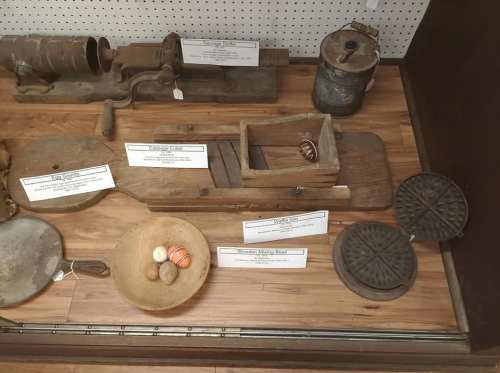 A display of vintage wooden tools and utensils, including a butter churn, bowls, and a wooden mold, on a wooden surface.