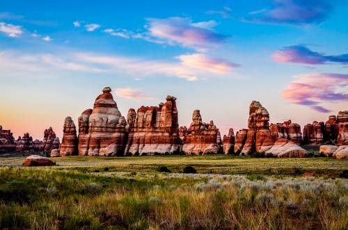 A stunning landscape featuring towering rock formations under a colorful sunset sky, with grassy plains in the foreground.