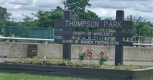Sign for Thompson Park in Middlesex County, featuring flowers and a cloudy sky in the background.
