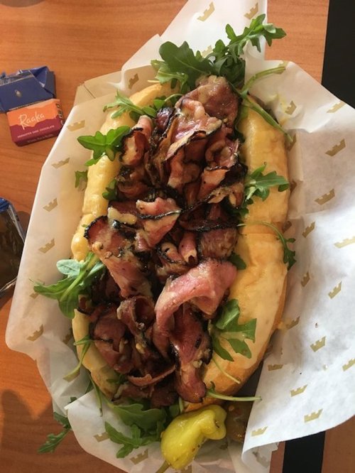 A large sandwich filled with sliced meats, arugula, and peppers, served in a soft, golden bun.