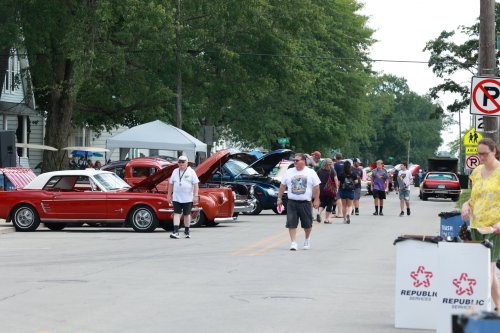 A street lined with classic cars and people walking, enjoying a car show on a sunny day.