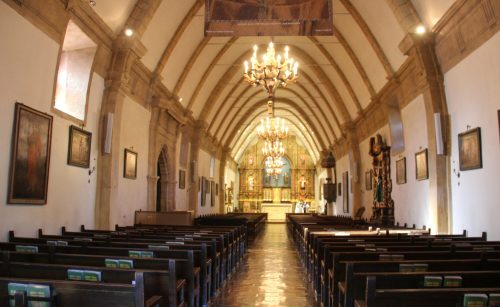Interior of a church featuring wooden pews, chandeliers, and ornate decorations along the arched ceiling.