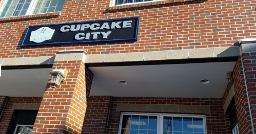 Sign for "Cupcake City" on a brick building, featuring a blue and white design above a storefront window.