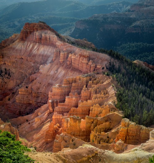 A stunning view of layered orange rock formations and green forests in a mountainous landscape.