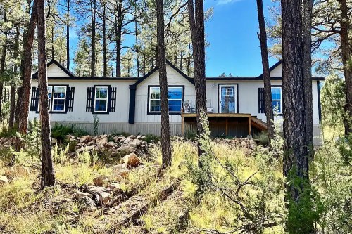 A modern house nestled among tall pine trees, featuring large windows and a wooden deck.