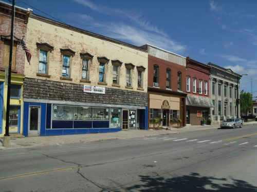 A row of historic buildings along a street, featuring various storefronts and a clear blue sky.
