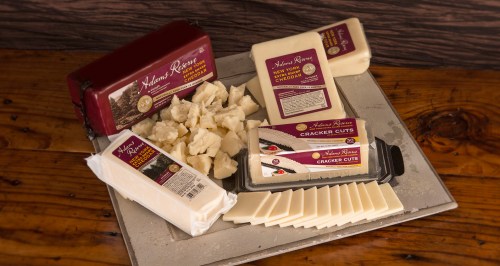 A wooden platter displays various cheese blocks and slices, including cheddar and cracker cuts, on a rustic background.