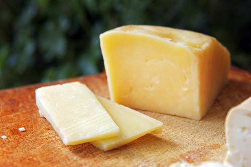 A block of yellow cheese with two slices cut from it, resting on a wooden cutting board.