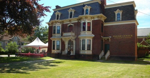 Historic brick building with a sign reading "Polish Center," surrounded by green lawn and a tent for events.
