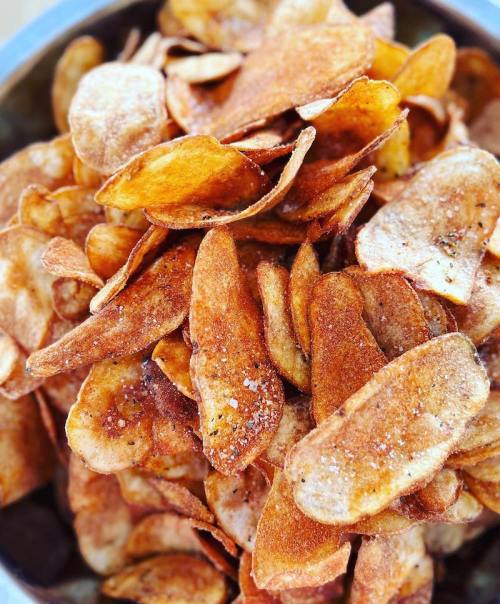 A close-up of a bowl filled with crispy, golden-brown potato chips, lightly salted and stacked.