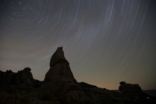 A night sky with star trails above unique rock formations, creating a serene and mystical landscape.