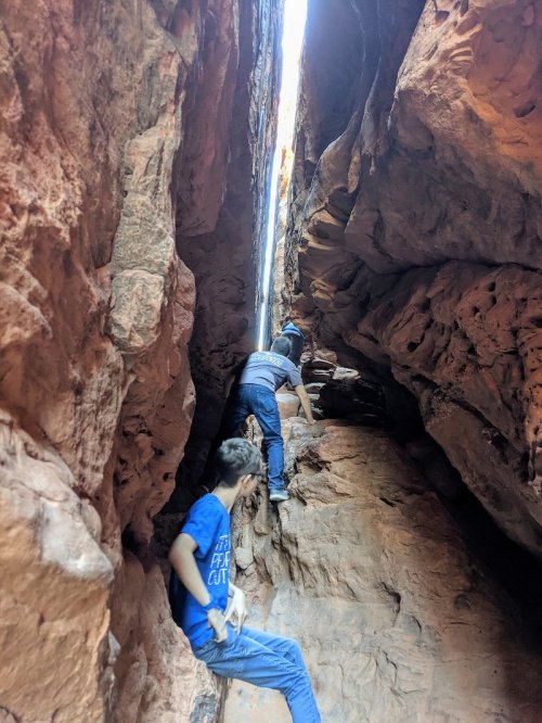 Two people climbing through a narrow rock crevice, surrounded by tall, rugged stone walls.