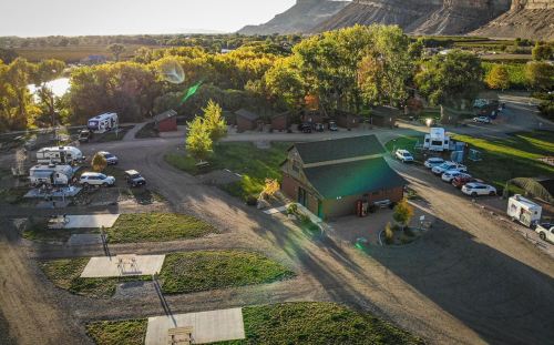 Aerial view of a campground with RVs, parked cars, and a main building surrounded by trees and mountains.