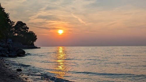 A serene sunset over a calm lake, with soft colors reflecting on the water and trees lining the shore.