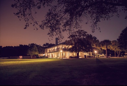 A well-lit building at night surrounded by trees and a grassy area, with a soft glow illuminating the scene.