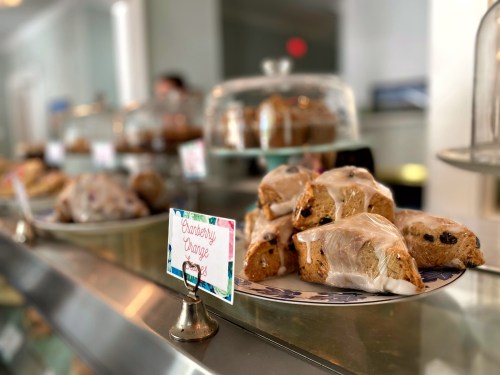 A display of baked goods, including scones, under glass domes with colorful labels in a bright café setting.