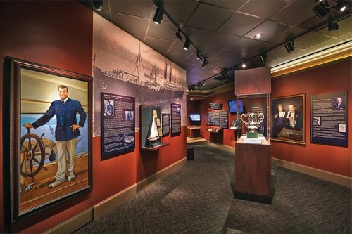 A museum exhibit featuring portraits, historical displays, and a trophy in a warmly lit room.