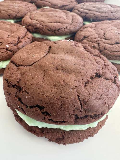 Close-up of a large chocolate cookie sandwich filled with green mint cream, surrounded by more cookies in the background.