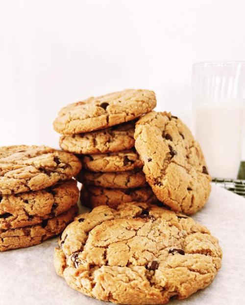 A stack of chocolate chip cookies next to a glass of milk on a white background.