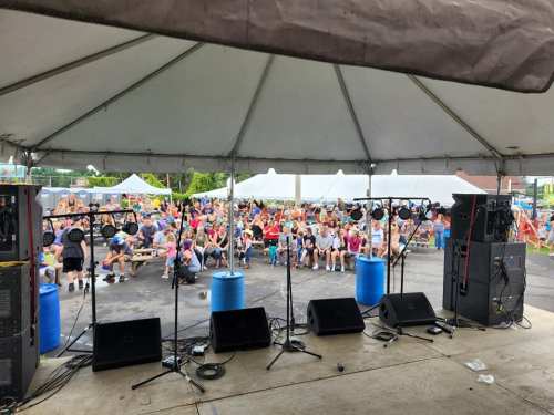 View from the stage at an outdoor event, with a large audience seated under a tent.