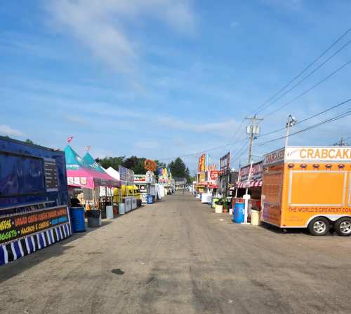 A wide view of a food truck alley with colorful stalls and tents lining both sides of a dirt path.