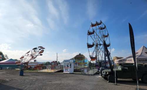 A fairground scene featuring a Ferris wheel and a spinning ride under a blue sky with scattered clouds.
