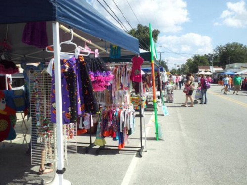 A vibrant street market with colorful tents displaying clothing and accessories, bustling with shoppers.
