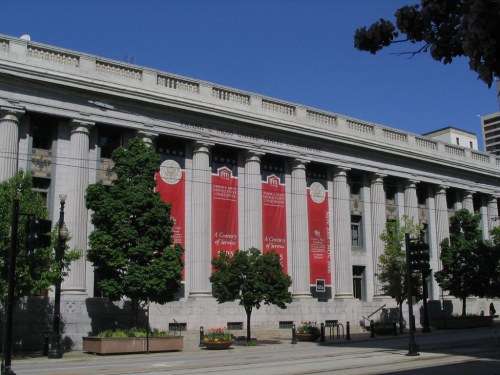 Historic building with tall columns, red banners, and trees lining the walkway under a clear blue sky.