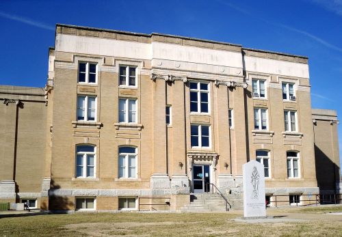 Historic brick building with large windows and a stone monument in front, set against a clear blue sky.
