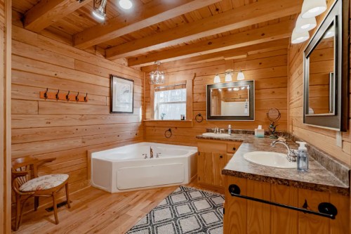 Cozy wooden bathroom featuring a large tub, double sinks, and rustic decor with warm lighting.