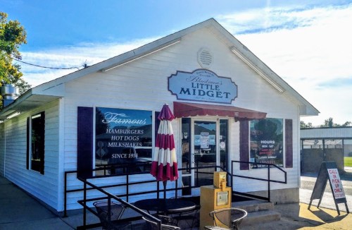A white building with a sign reading "Anderson's Little Midget," featuring outdoor seating and a menu of burgers and shakes.