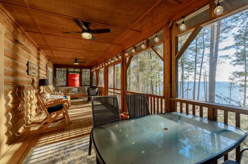 Cozy screened porch with a table and chairs, overlooking a lake and surrounded by trees. Warm, inviting atmosphere.