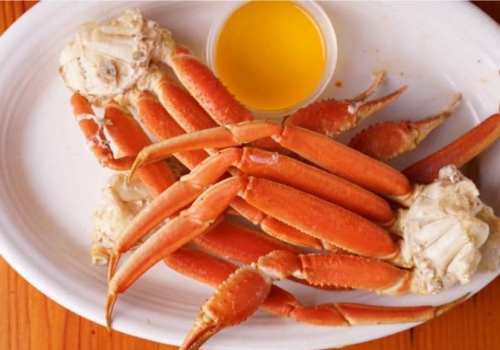 A plate of cooked crab legs served with a small dish of yellow dipping sauce.