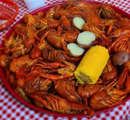 A large platter of spicy crawfish, potatoes, and corn on a red and white checkered tablecloth.