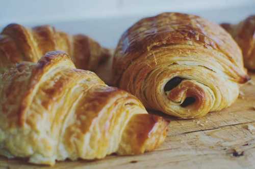 Freshly baked croissants on a wooden surface, showcasing their flaky, golden layers.