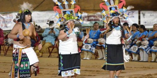 Three dancers in traditional attire perform at a cultural event, showcasing vibrant costumes and accessories.