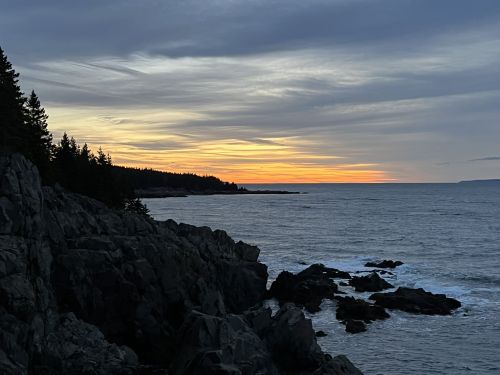 A serene coastal scene at sunset, with rocky shores and a colorful sky over the calm ocean.