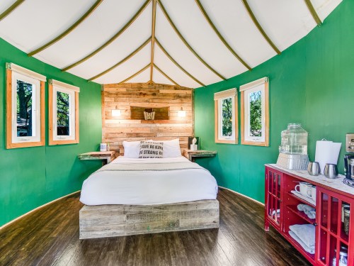 Cozy yurt interior with green walls, wooden accents, a bed, and a small kitchenette area. Bright and inviting atmosphere.