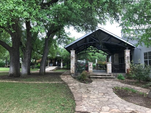 A stone pathway leads to a covered patio surrounded by trees and greenery, creating a serene outdoor space.