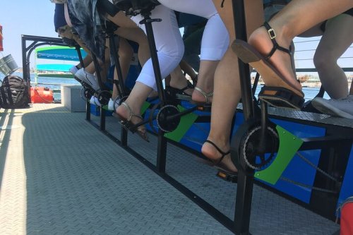 A group of people pedaling on a watercraft, showcasing their legs and feet in sandals.