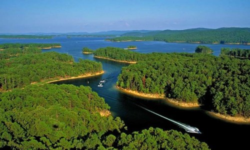 Aerial view of a serene lake surrounded by lush green forests and small islands, with boats navigating the water.