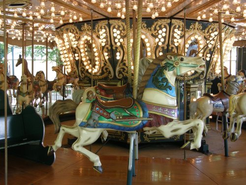 A colorful carousel with ornate horses and bright lights, set in a lively amusement park atmosphere.