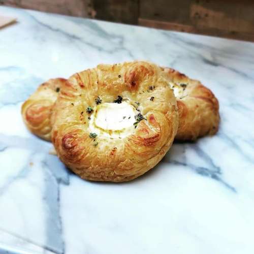 Three golden, flaky pastries with a creamy filling, garnished with herbs, resting on a marble surface.