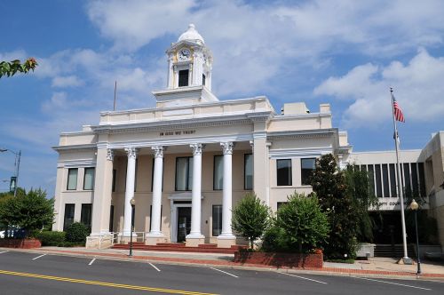 Historic courthouse with a clock tower, columns, and a flag, set against a blue sky with scattered clouds.