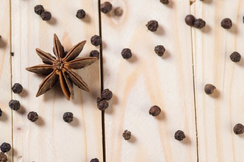 Star anise and black peppercorns scattered on a wooden surface.