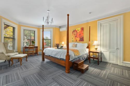 Cozy bedroom with a four-poster bed, yellow walls, a chandelier, and a seating area by the window.